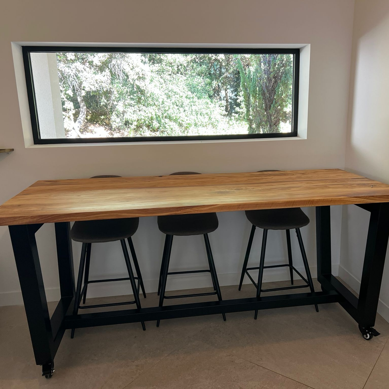 Détail du piètement trapézoïdal en acier noir et des roulettes de la table AIX.