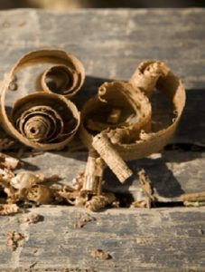 Gros plan sur des copeaux de bois massif bruns et bouclés, issus de la taille artisanale d'un plateau de table, évoquant la texture et le parfum du bois brut fraîchement travaillé.
