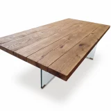 Gros plan sur le plateau en chêne massif au toucher rustique et brossé de la table MENTON, montrant la fixation discrète du pied en verre.